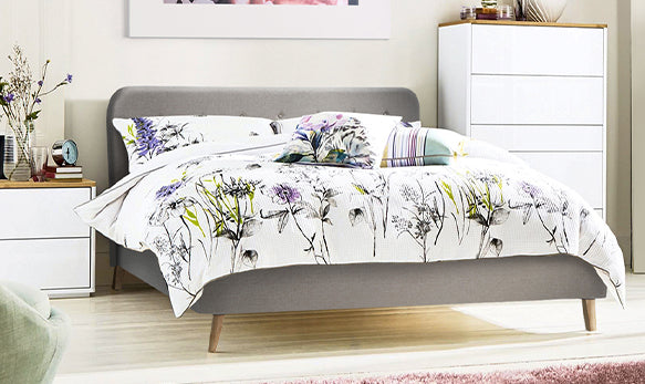 A grey fabric upholstery bed frame in queen size stands out in a bright, contemporary bedroom. 