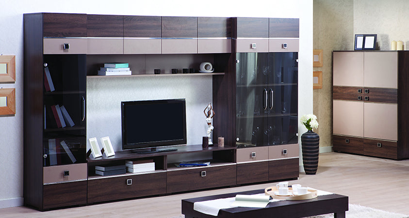 A dark wood grain and glass entertainment centre. The glass cabinets are holding several books on the left, and a set of drinking glasses on the right. The open shelves contain books, picture frames and other household decorations, as well as a medium sized plasma TV. The room features a matching cabinet in the right corner, and a black coffee table holding a tea set and white table runner.