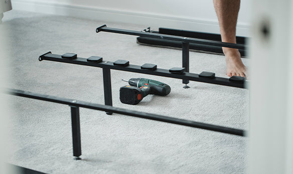 A man assembling a bed frame in an empty bedroom.