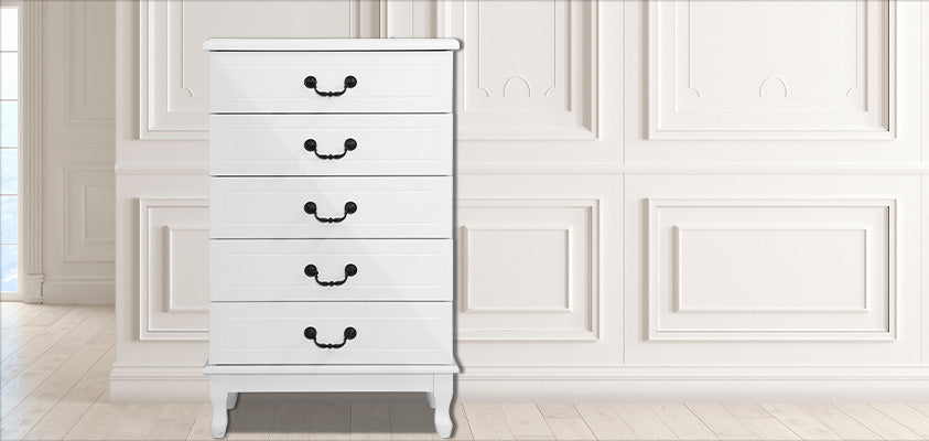 An Artiss 5 drawer white provincial style tallboy with black handles, in a white room with moulded wall panels.