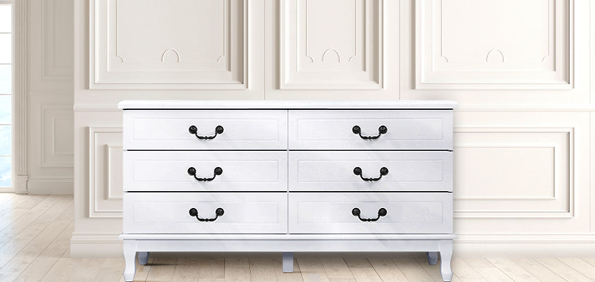 An Artiss 6-drawer white provincial style lowboy set in a white room with moulded wall panels.