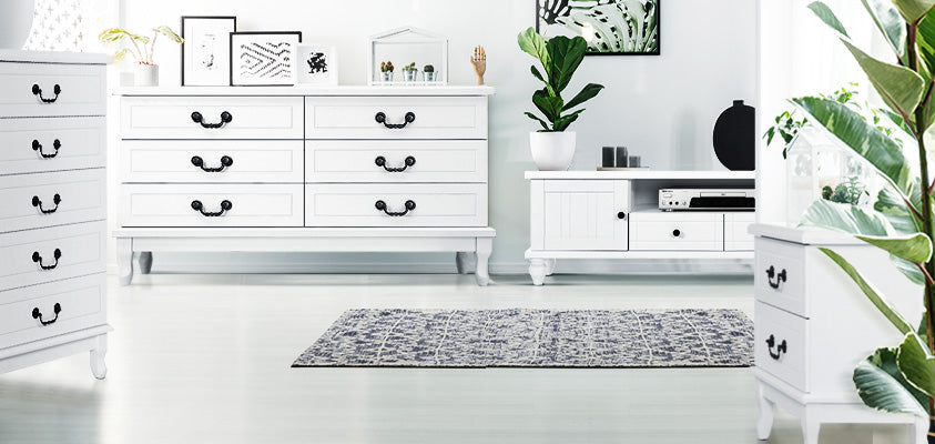 A lounge room outfitted with matching Artiss white provincial style furniture. It features a tallboy, a lowboy, a bedside table, an entertainment unit, and an Artiss blue patterned rug. They are decorated with various green plants and black and white artworks.