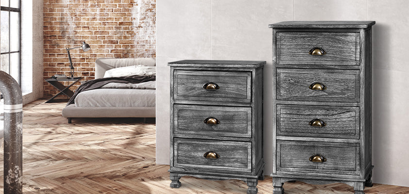 Two Artiss grey vintage chests of drawers, one 3-drawer and one 4-drawer, with brass fittings. They are set against a concrete wall around the corner from an industrial style bedroom
