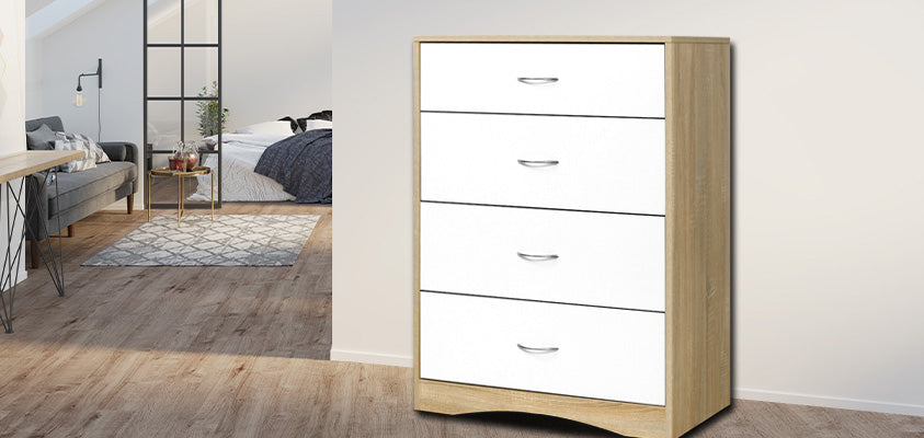 An Artiss 4-drawer white and wood tallboy. It is set against a beige wall around the corner from a grey living room setting that extends into a bedroom. 