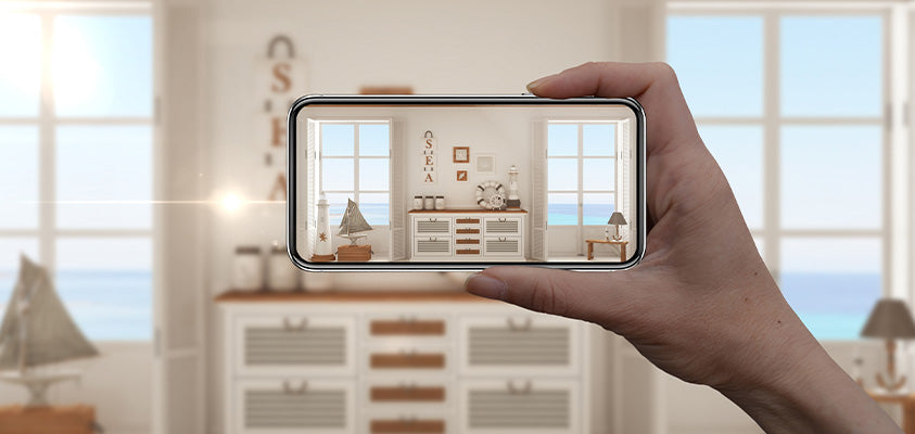 A person taking a picture of their living room setting, which is decorated in a costal style with white and wood furniture.