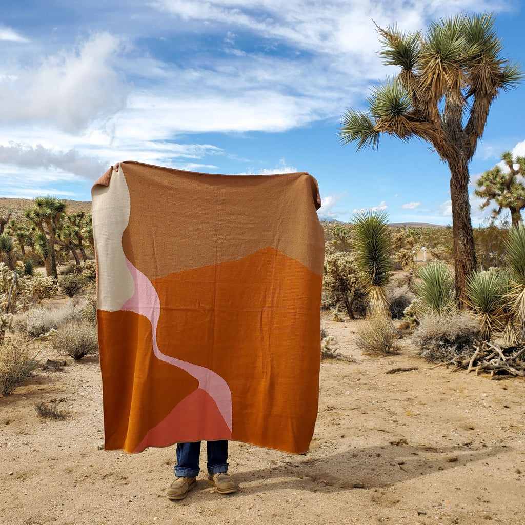 Pink, orange, and brown blanket held up by a person in the desert
