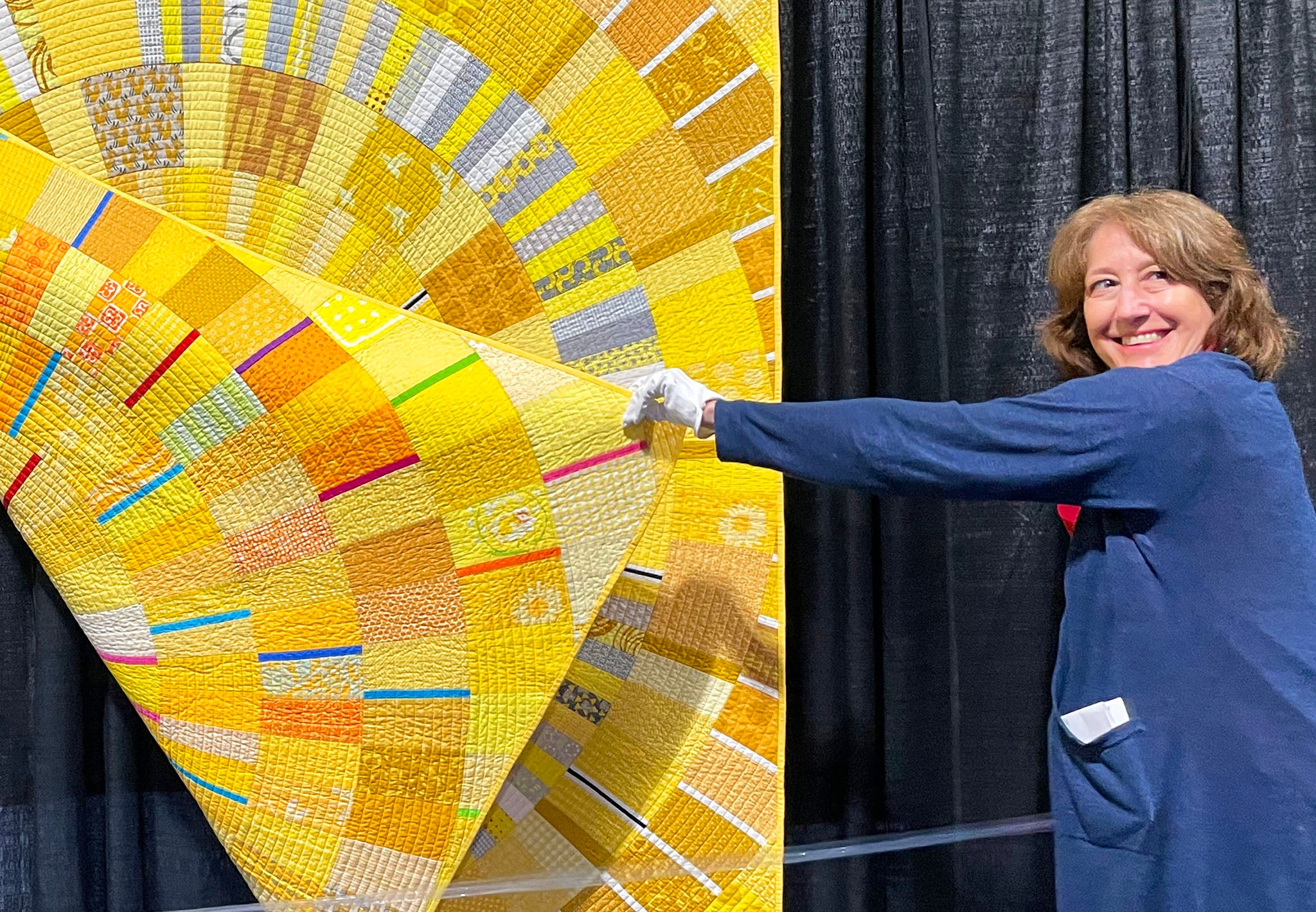 Long Beach Quilt Festival 2023 - White Glove Attendant Leia showing the back of Turn the Dial by Kathy York - Photo By Victoria Stone