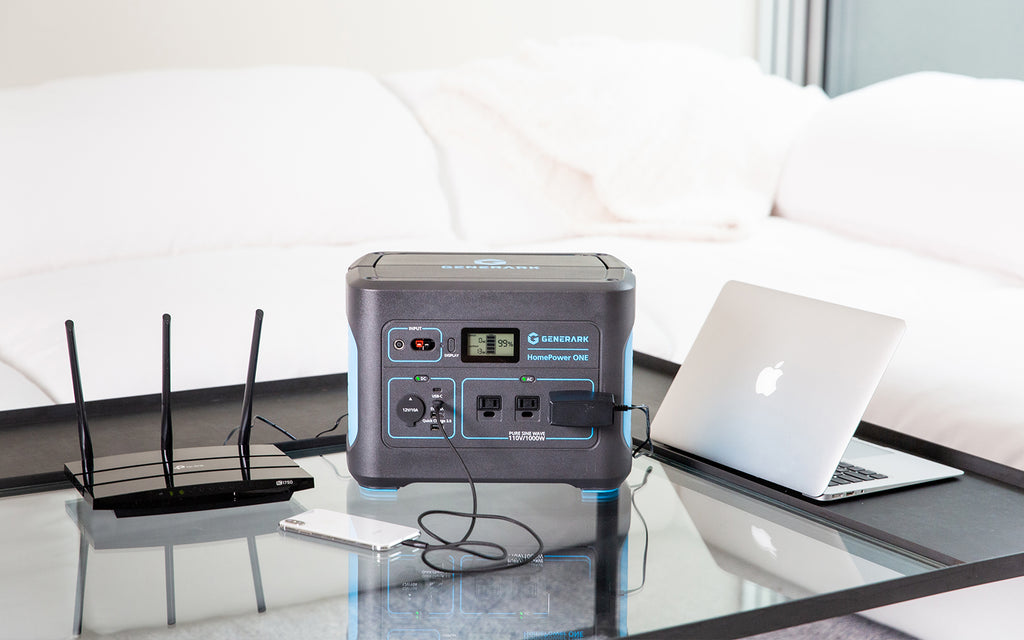 The HomePower ONE backup battery generator is pictured on a coffee table powering a modem, cell phone, and laptop.