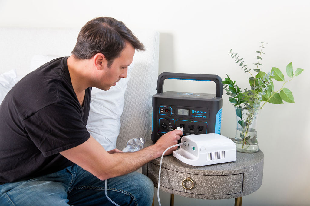 A man sits on a bed and plugs a CPAP machine into the HomePower ONE portable power station.