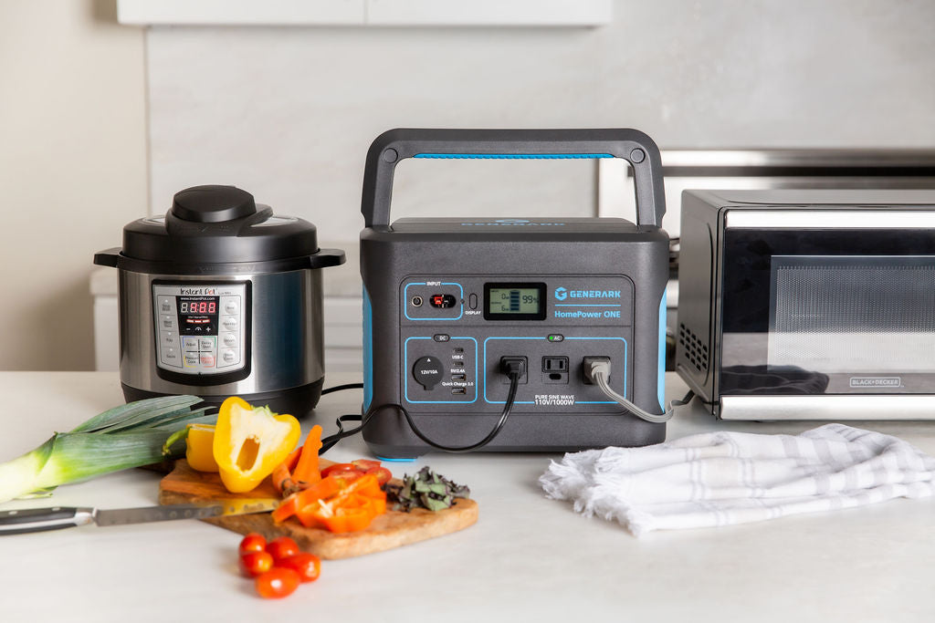 The HomePower ONE portable power station is pictured on a kitchen counter powering a slow cooker and microwave with sliced vegetables also on the counter.