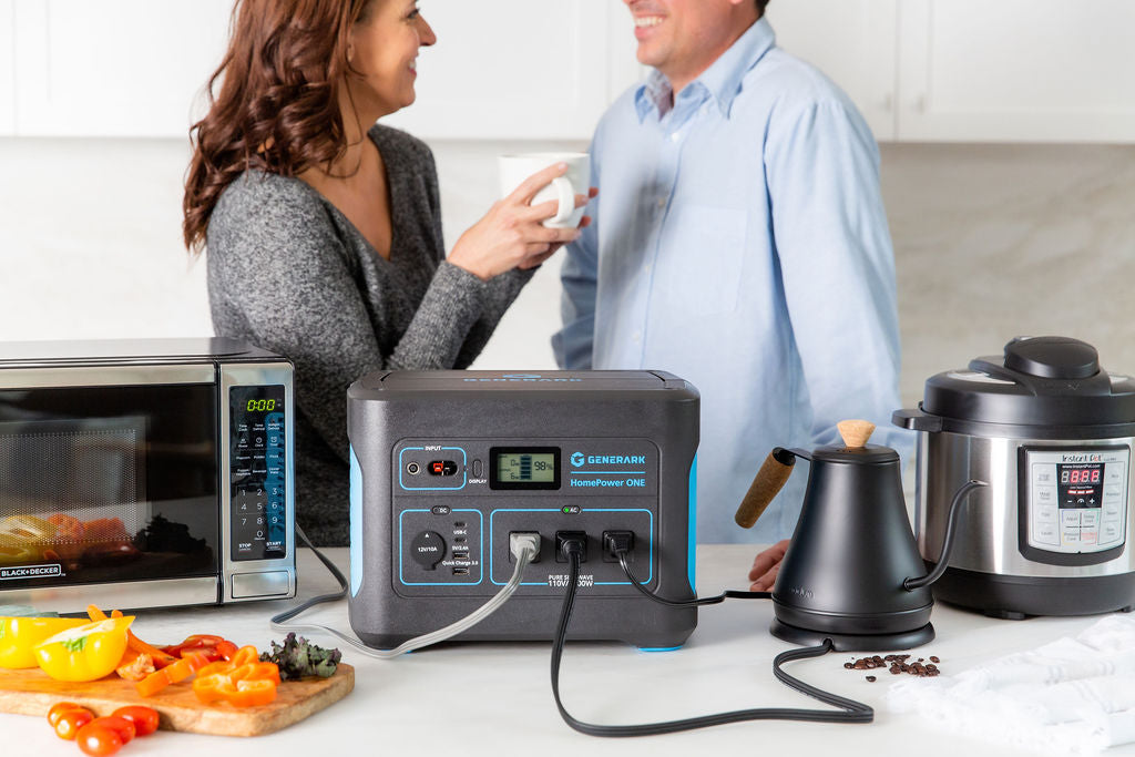 A man and women have a conversation in the kitchen with the HomePower ONE backup battery power station that is powering a microwave, kettle, and slow cooker.