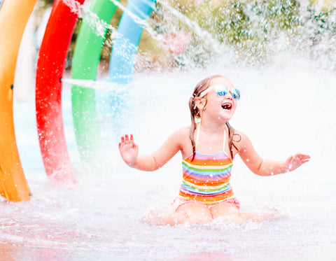 Girl Kneeling in Water Under Sprinklers at Splash Pad