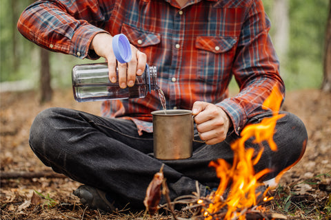 man sitting by a fire drinking water 