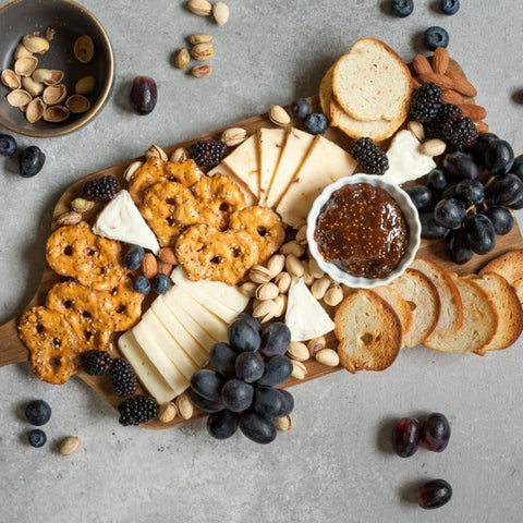 Charcuterie board with cheeses, crackers, fruits and spreads on wood serving board