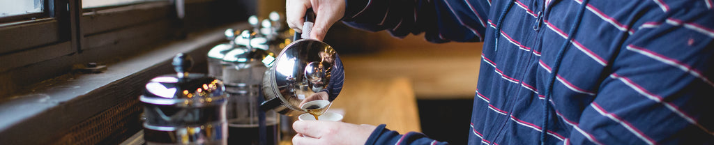 man pouring from a french press with other coffee brewers behind him in background