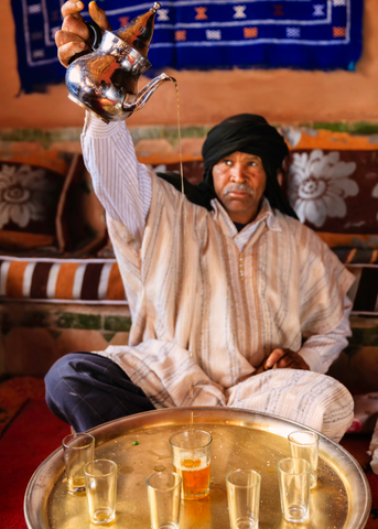 Homme marocain servant du thé à la menthe du Maghreb dans des tasses en verre en hauteur