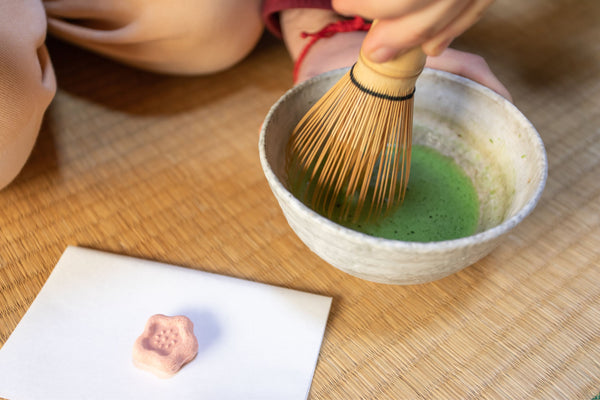 bowl of matcha being whisked next to sakura sweet