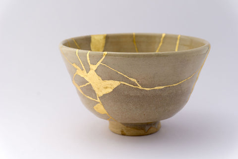 tan colored tea bowl with gold kinsugi repairs