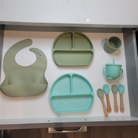 a kitchen drawer organized with baby's tableware such as silicone bibs, plates, sippy cups and utensils