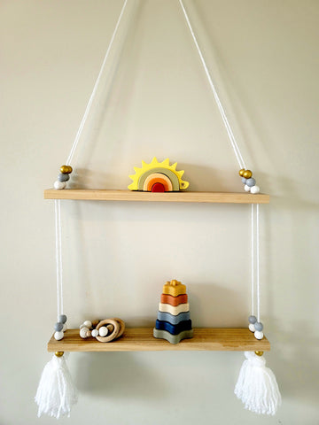 A hand made wooden hanging shelf with montessori baby toys on it hung on the wall