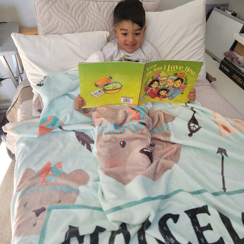 baby boy in bed reading a book while covered with a personalized baby fleece blanket