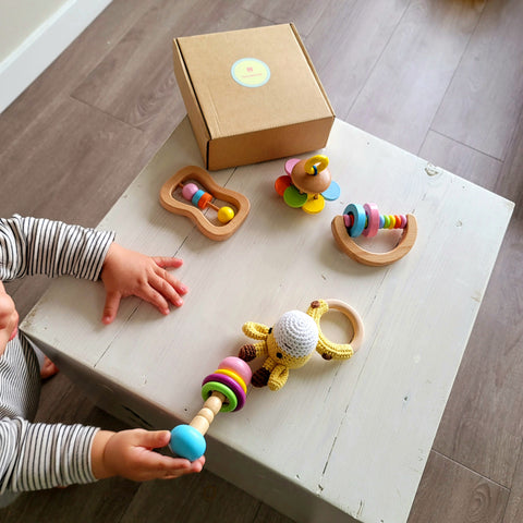 Baby playing with a wooden montessori baby set with rartles on top of a baby sized table