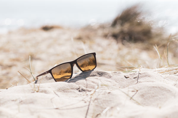 Polarised sunglasses lay on a sandy beach