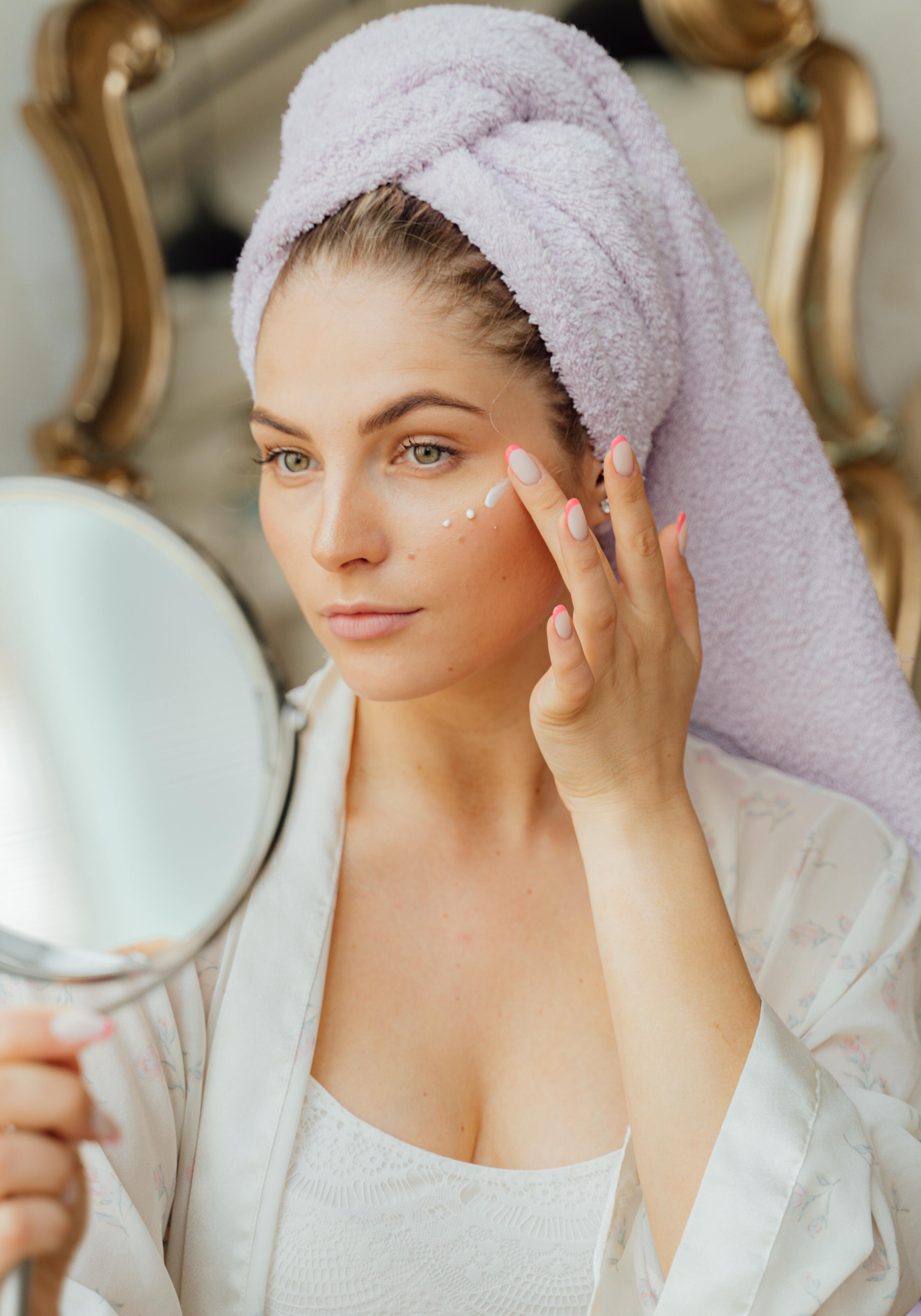 A woman looking into a hand mirror and applying primer on her face