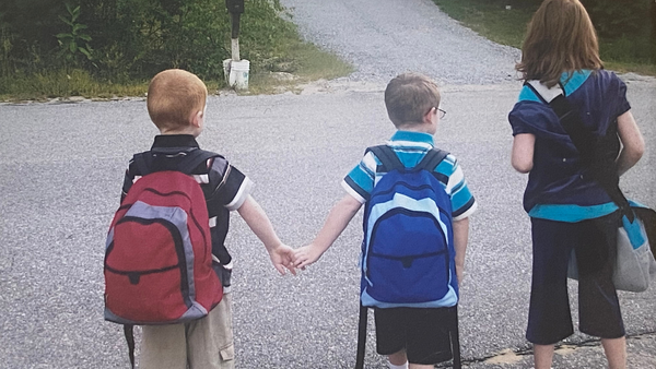 twin brothers waiting at the bus stop, holding hands and waiting with big sister to go to kindergarten