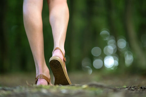 back of a woman's legs walking forward in sandals on green grass