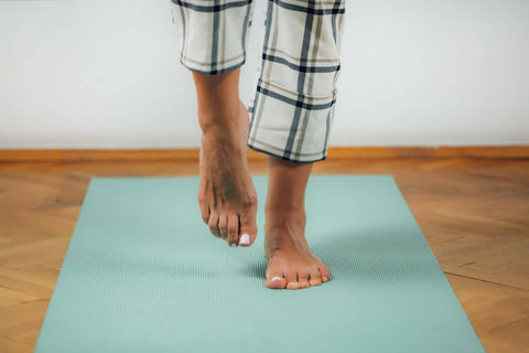 Man standing on yoga mat in bare feet with right foot raised
