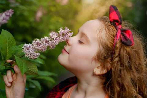 young red-haired girl with head back sniffing lilac