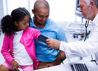 African American father holding daughter with Doctor taking her blood pressure