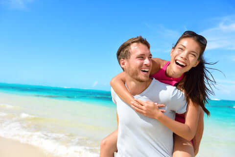 Man holding woman on his back on the beach both smiling