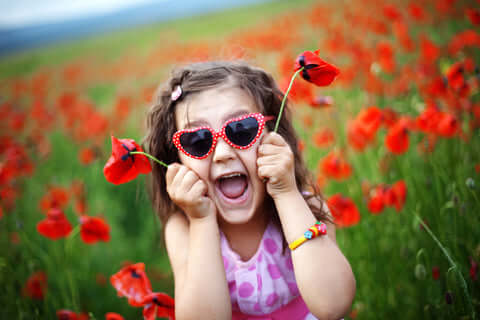 girl with heart shaped sunglasses in field of red flowers