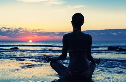 person meditating on beach facing sunset