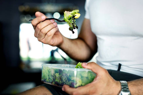 man's hands holding bowl with salad and forkful of salad he is getting ready to eat