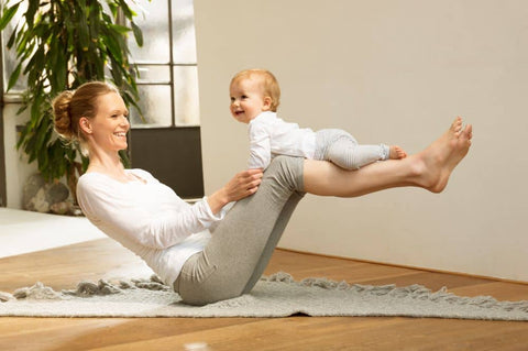 woman balanced on floor, head and legs raised, smiling at baby on her knees