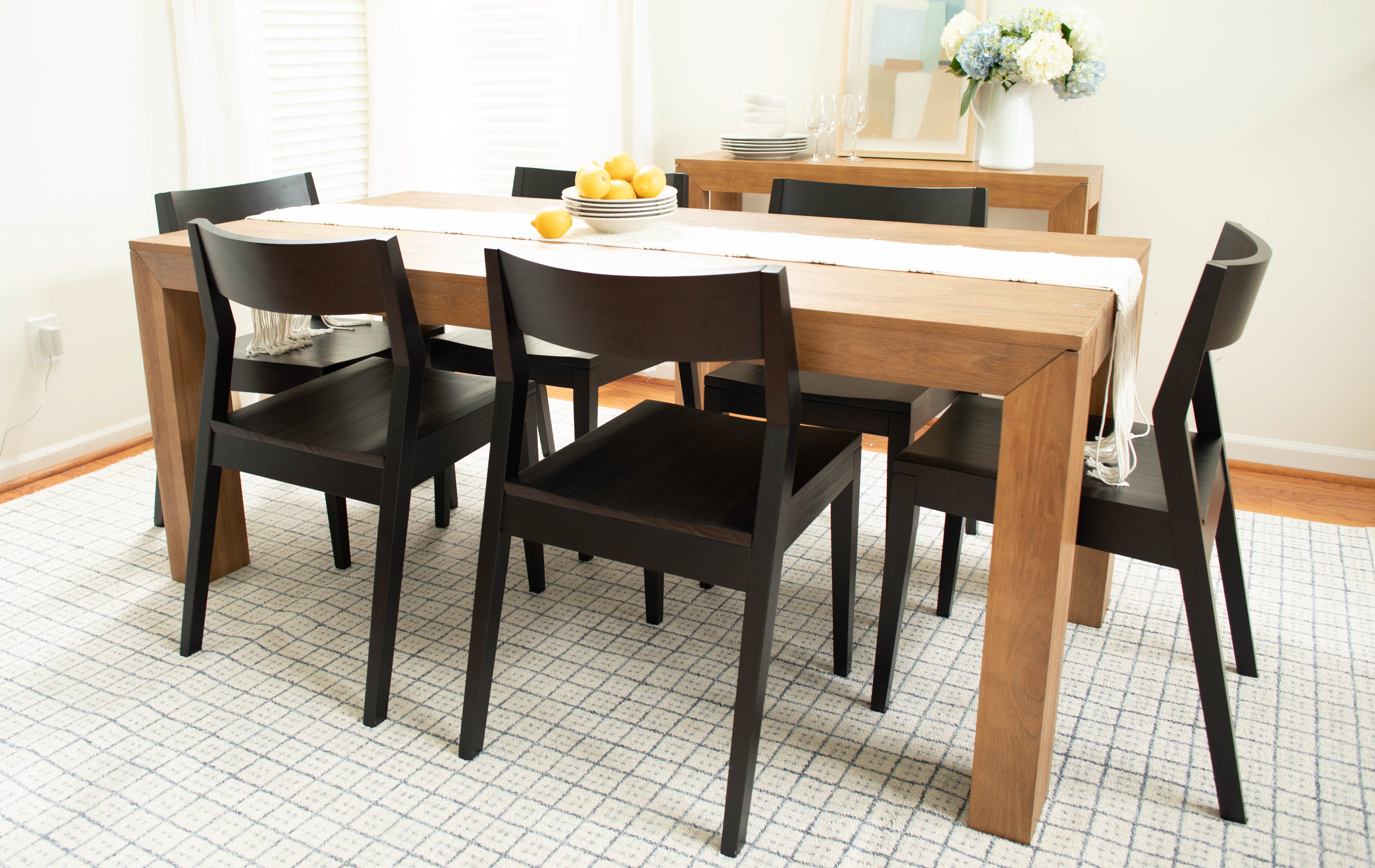 Modern dining table in pecan with solid wood black dining chairs, rug, table runner, lemon centerpiece, and decorative flowers