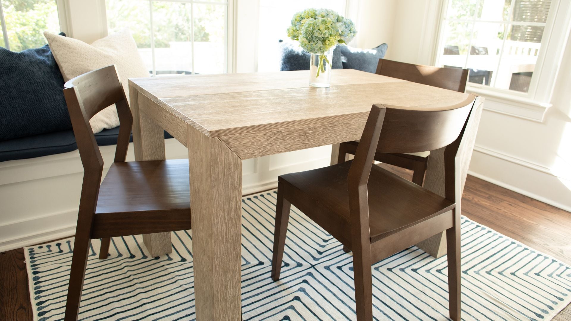 Solid Wood Modern Dining Table and Chairs with Banquette, Striped Rug, and Floral Centerpiece