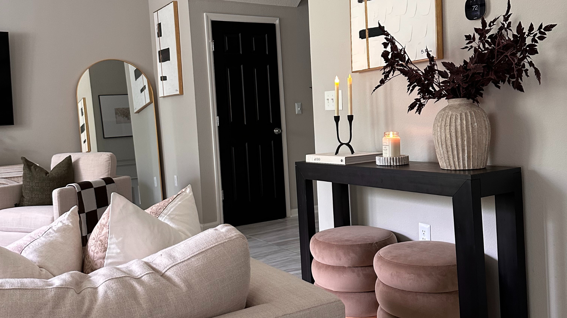 Modern black console table with vase, candles, and ottomans underneath and light pink couch