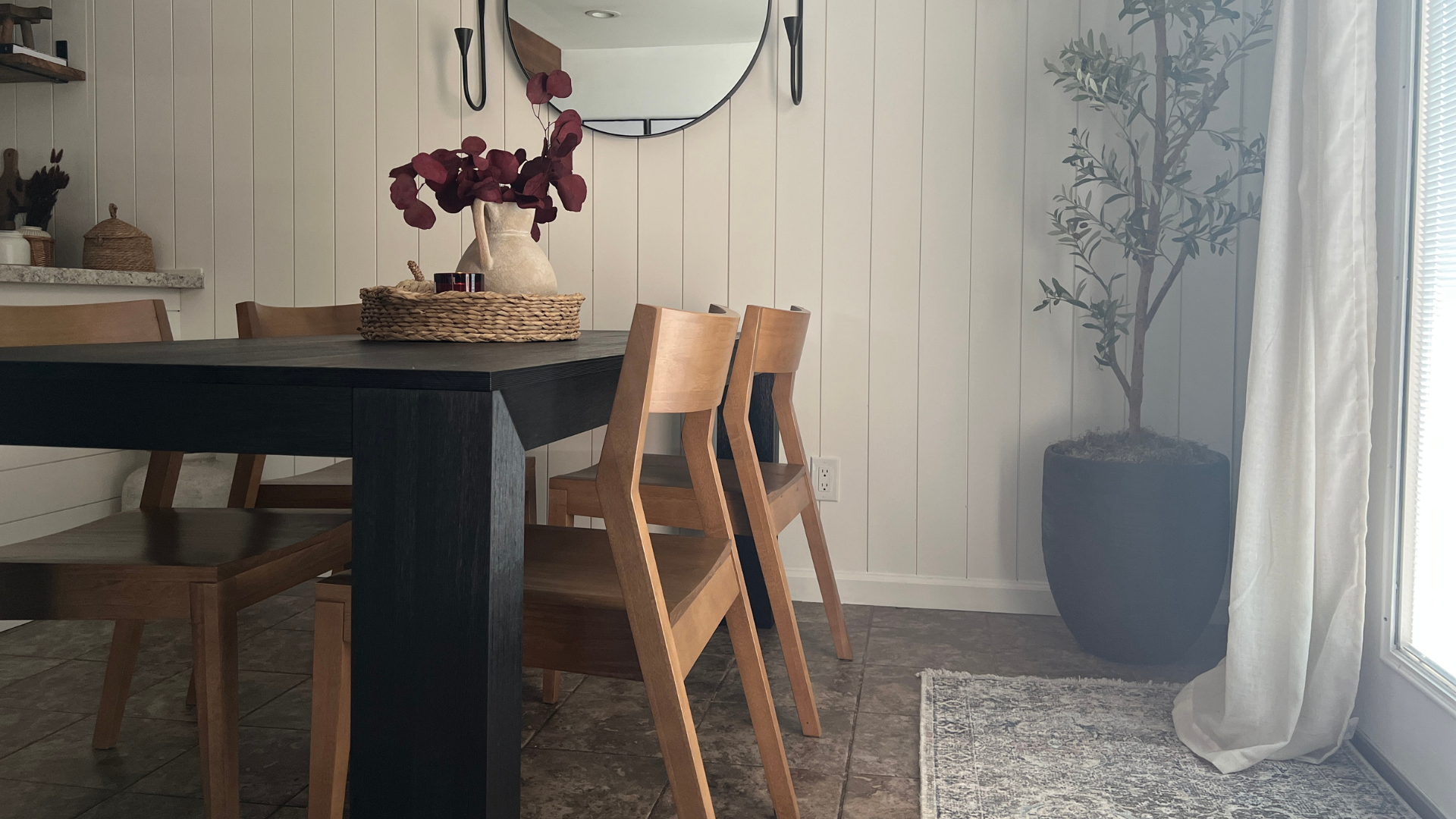 Modern black dining table with solid wood dining chairs in pecan, floral centerpiece, and round mirror