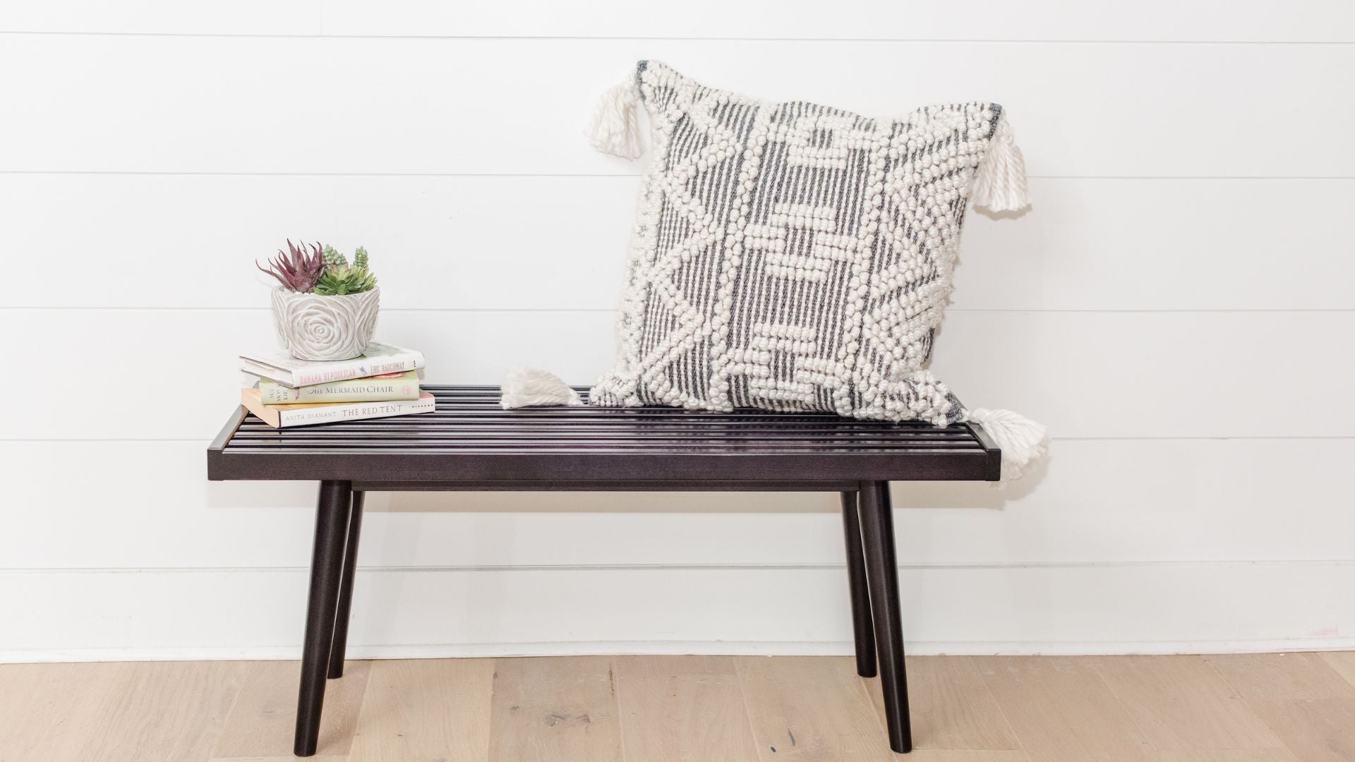Solid wood black entryway bench with books, pillow, and plant