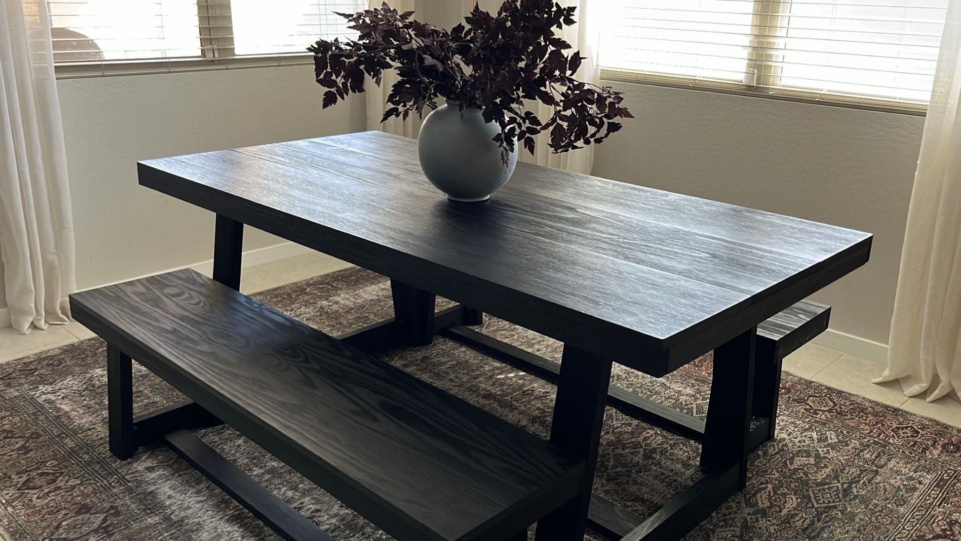 Black Dining Table Set with Two Dining Benches, Plant Centerpiece, Brown Rug, and Decor