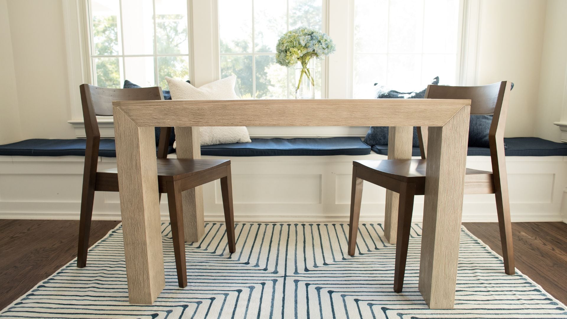 light wood dining table with walnut dining chairs and floral centerpiece in breakfast nook