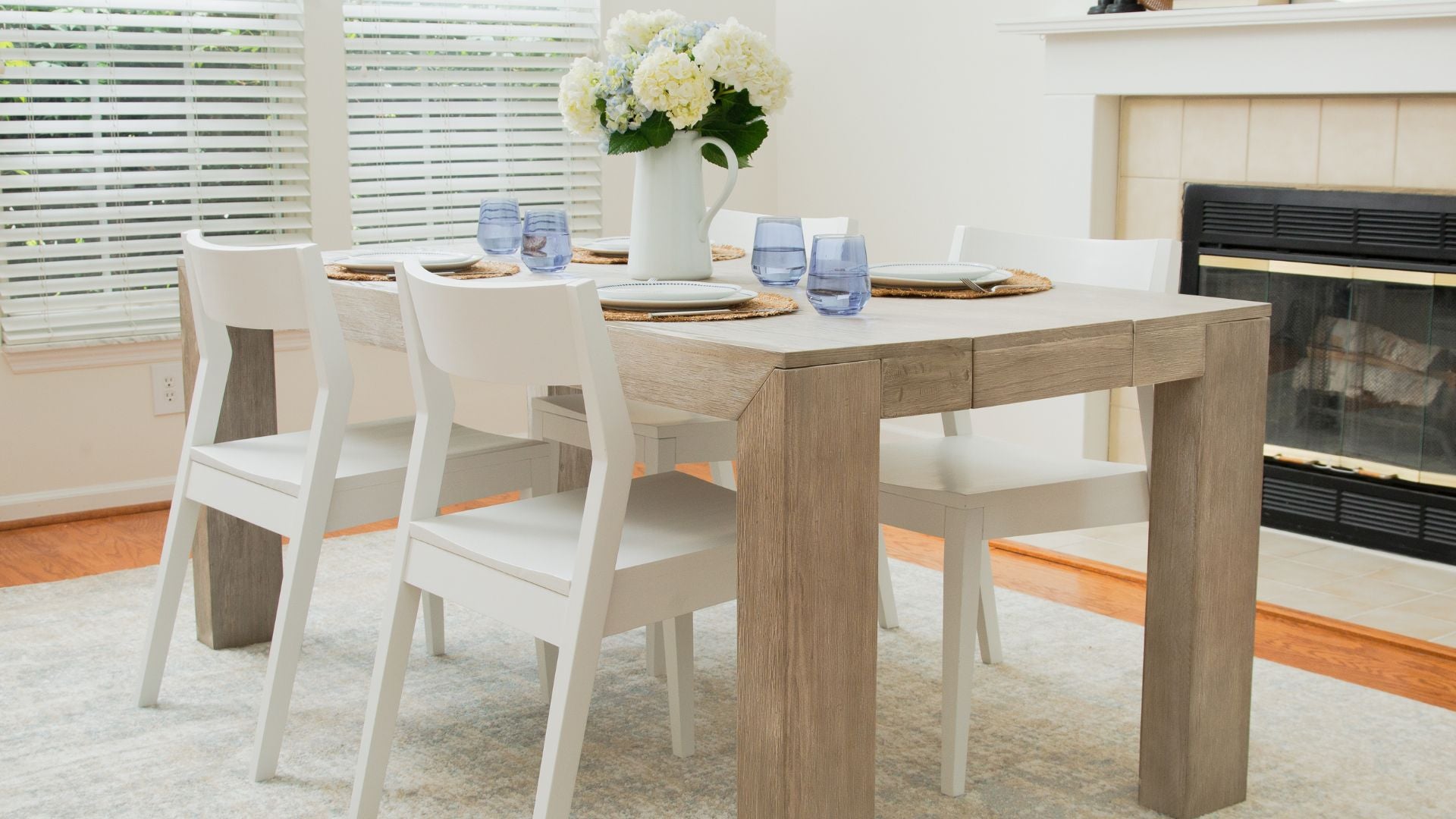 light wood dining table and white dining chairs with floral centerpiece and blue glassware