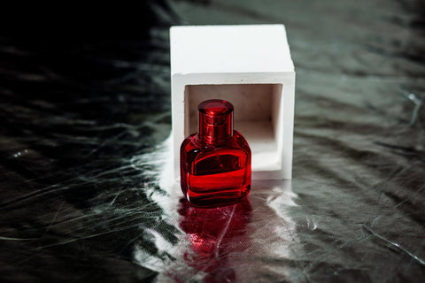Frasco de perfume rojo cerca del cubo blanco