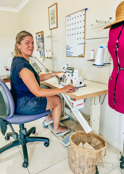 Sara, the designer, sitting at her sewing desk looking at the camera and smiling