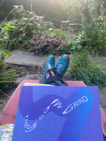 POV of the slow grind book with feet and a garden in the background
