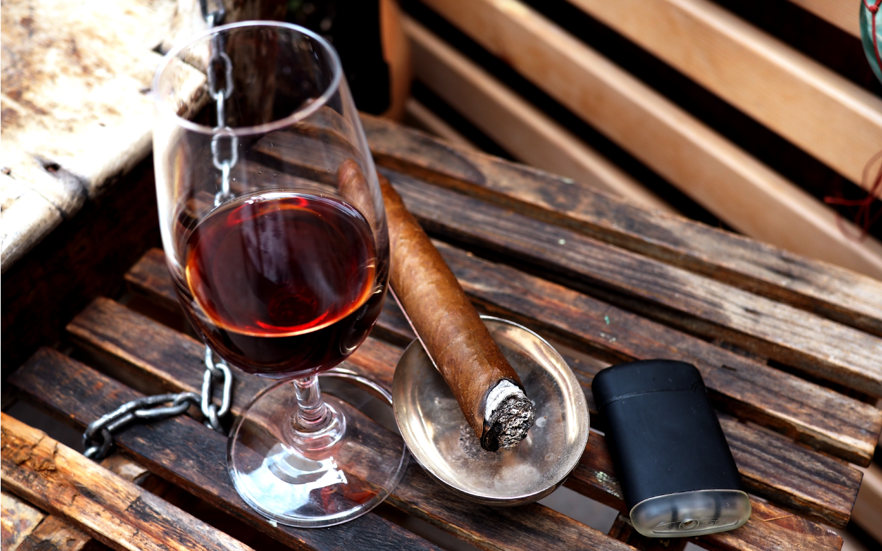 Image of a glass of wine setting next to a lit cigar in an ash tray